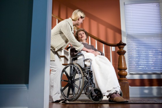 Female nurse helding elderly woman in wheelchair at home